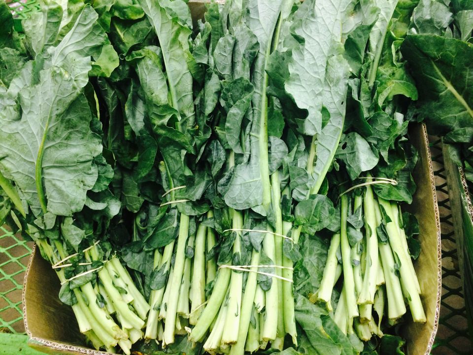 Bundles of fresh green leafy vegetables, including chard and collard greens, on display