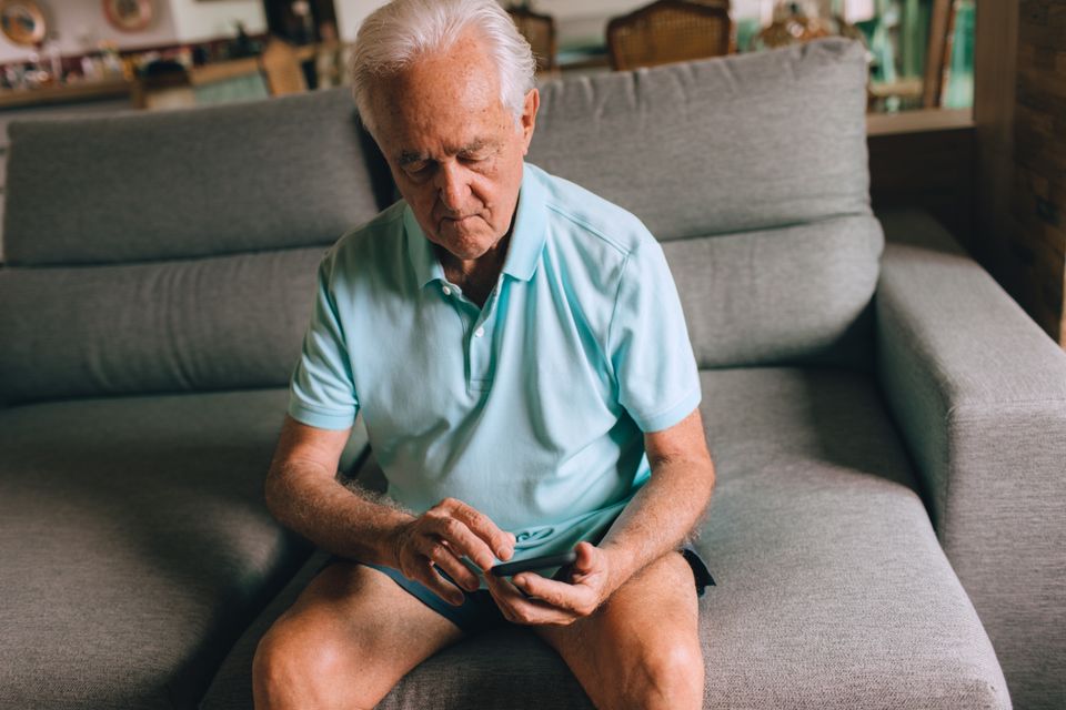 Elderly man sitting on a sofa in a cozy living room using a smartphone