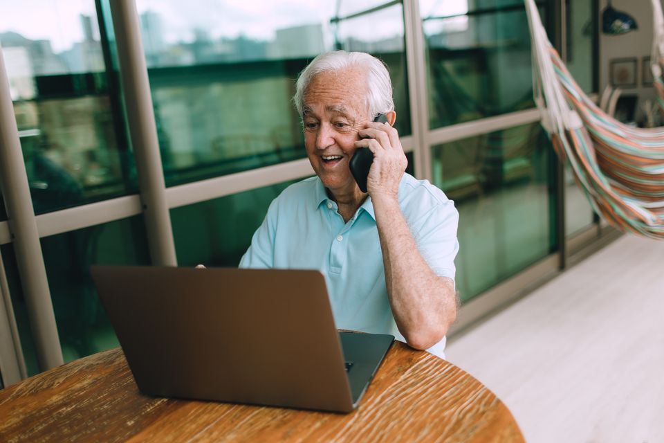 Elderly man in casual setting using a laptop and smartphone indoors