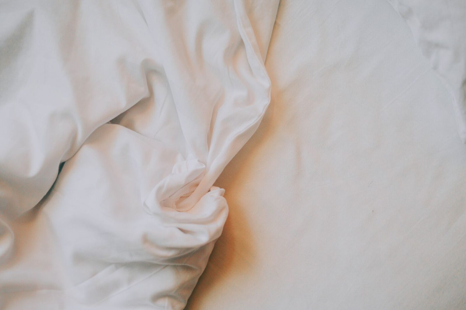Close-up texture of soft, crumpled white cotton bed sheets fresh from the wash