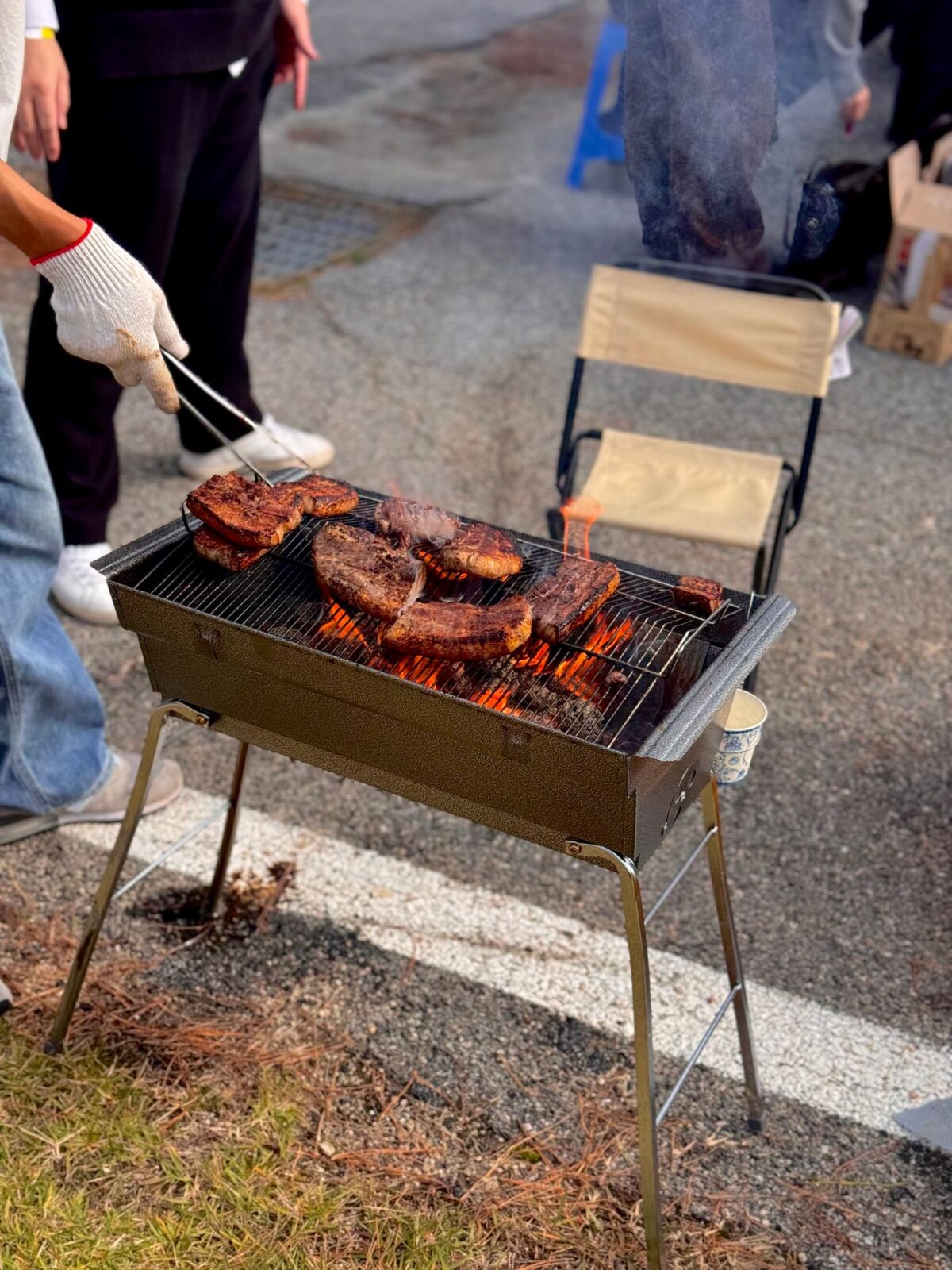 Person grilling steaks on a portable propane grill outdoors on a summer day