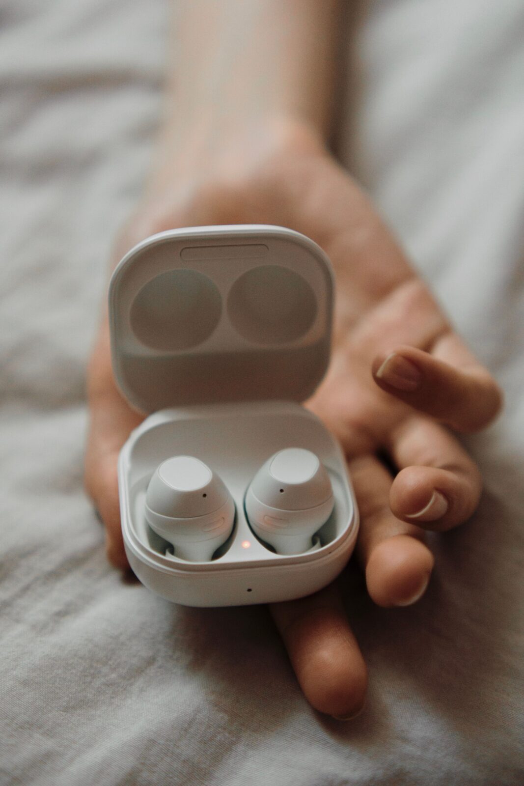Compact wireless earbuds resting in an open charging case held in an adult's hand