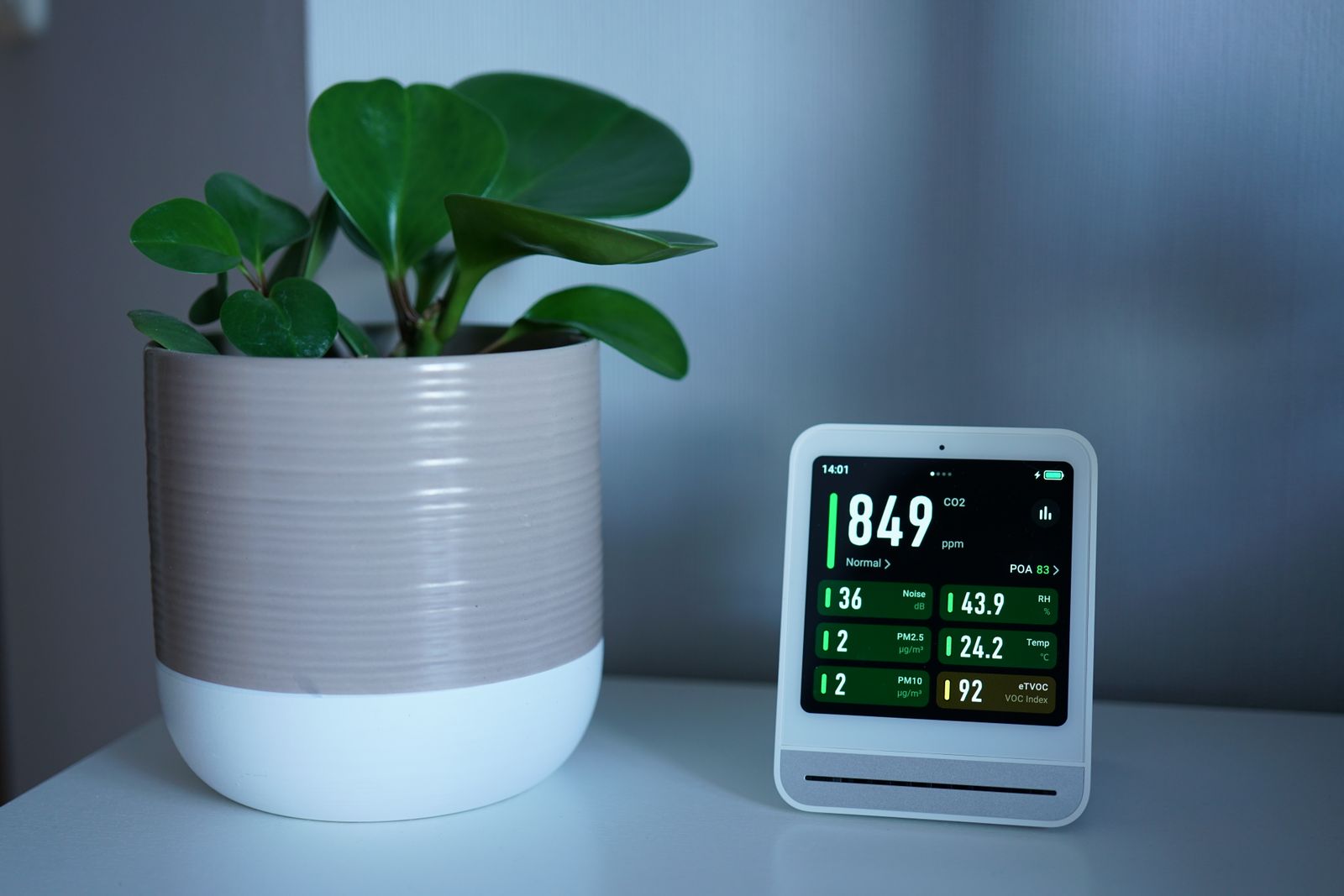 An air quality monitor displaying readings next to a potted plant on a desk