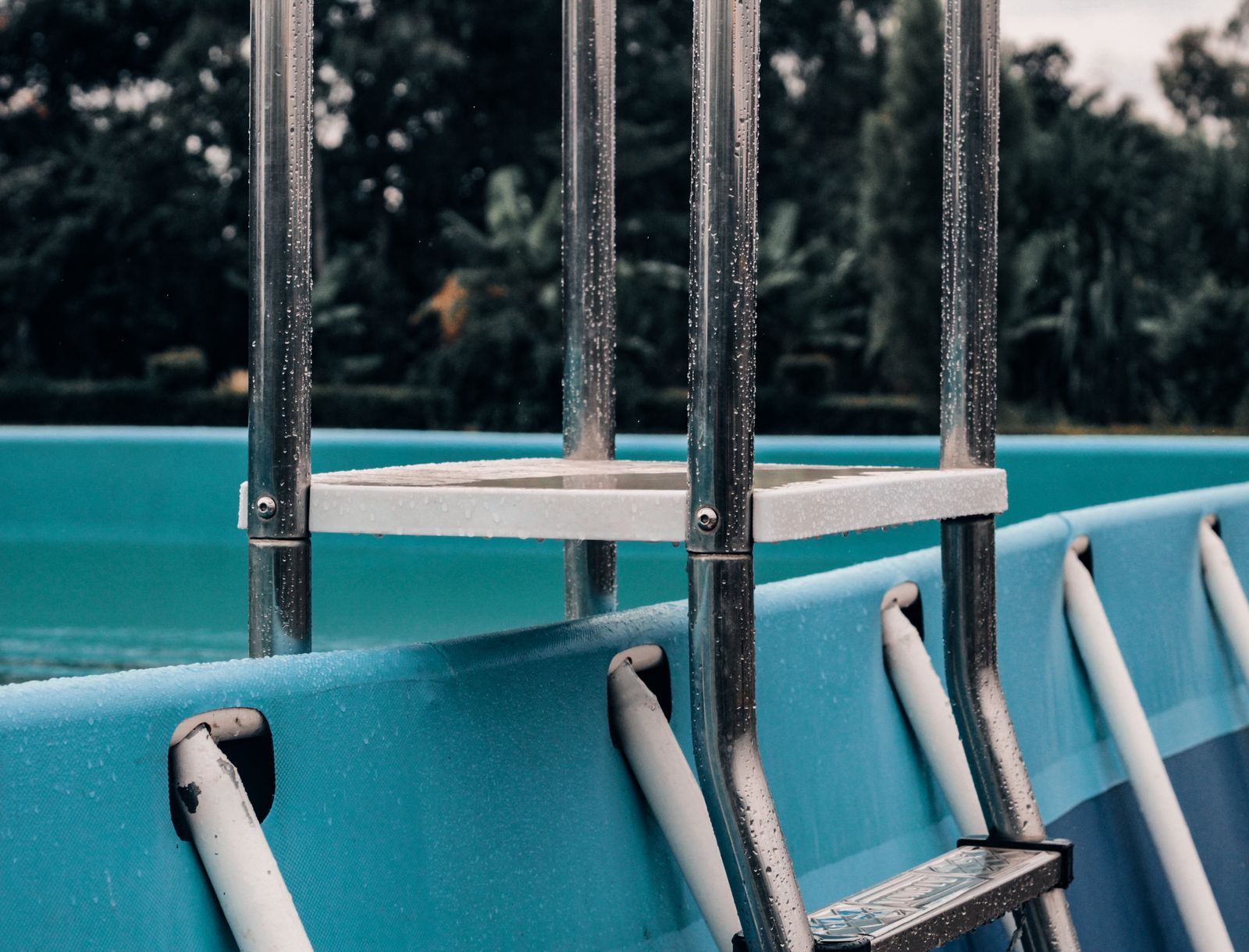 Close-up of a wet metal ladder entering an above-ground backyard pool