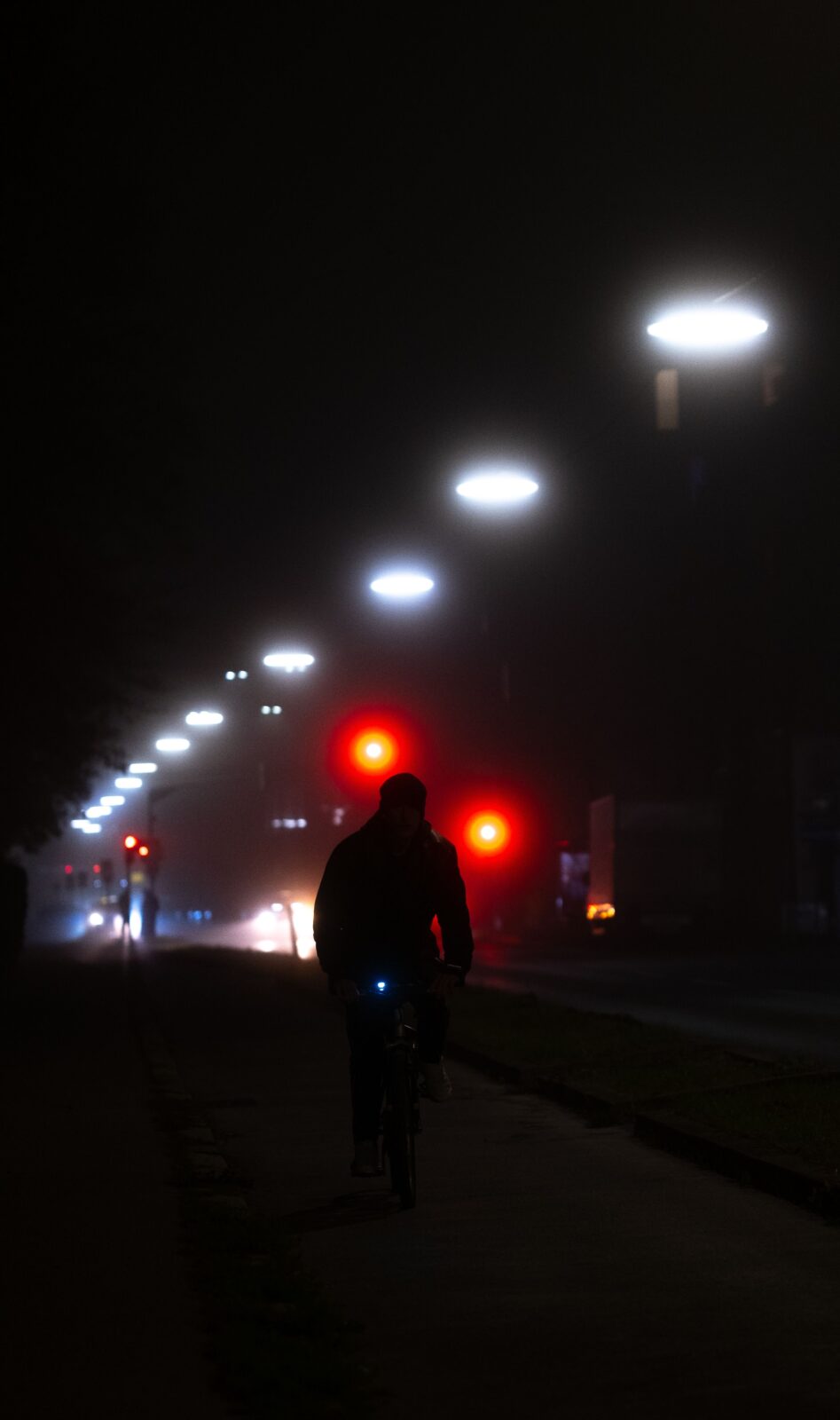 A cyclist silhouetted riding through a foggy urban street at night under glowing streetlights