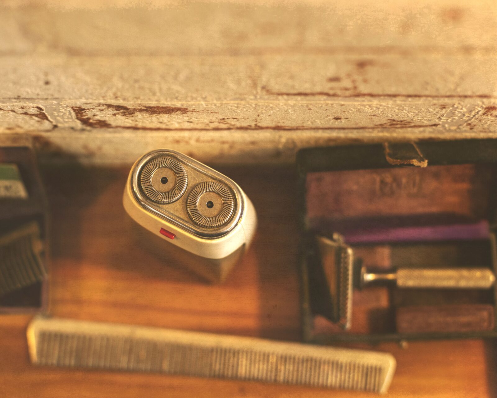 Electric rotary shaver with round cutting heads resting beside a comb and a safety razor on a wooden surface