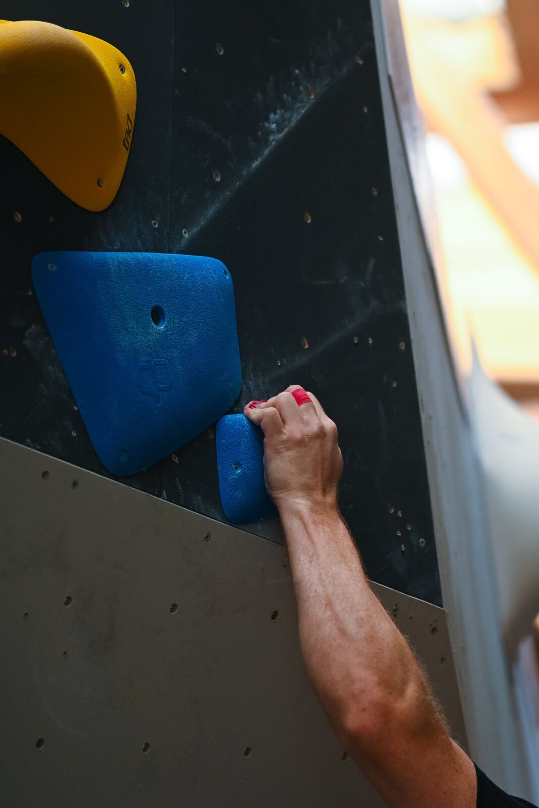A climber's hand firmly gripping a blue climbing hold on an indoor bouldering wall