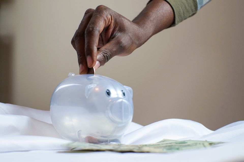 Close-up of a person's hand placing coins into a transparent piggy bank