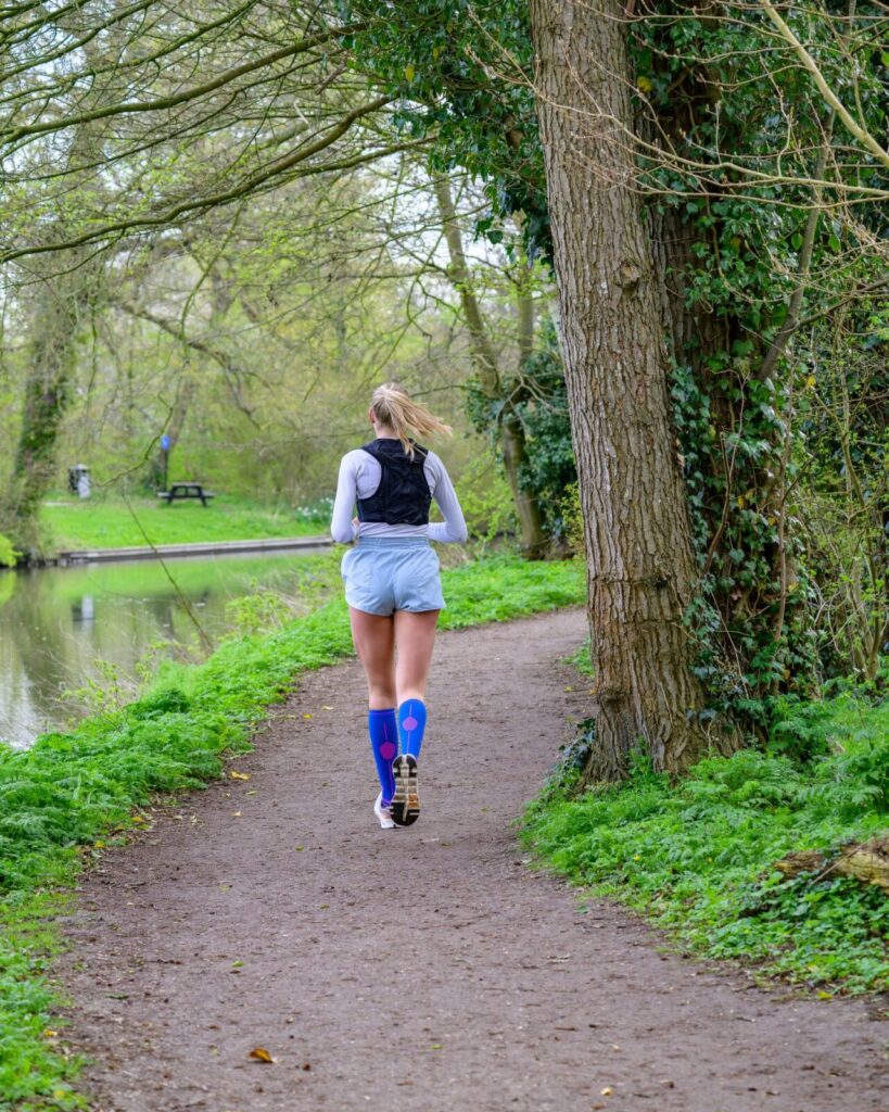 Runner in calf-length compression socks on a wooded trail beside a river