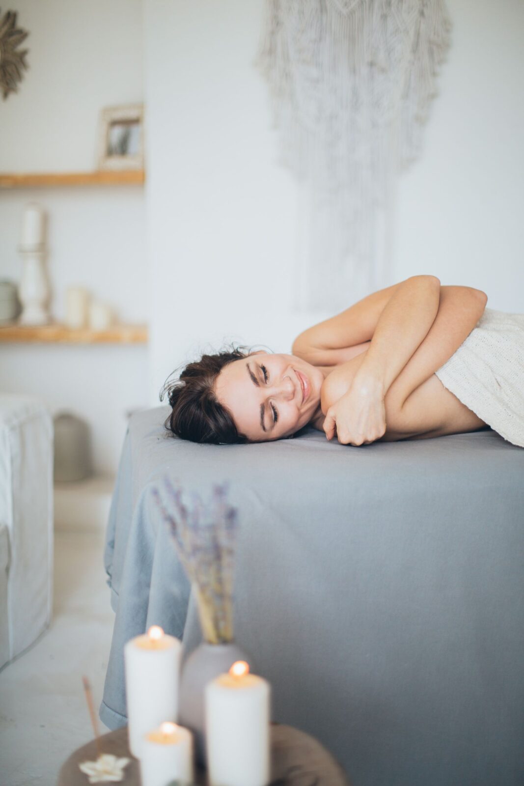Woman wrapped in a towel relaxing on a massage table, representing the at-home relaxation personal infrared sauna blankets aim to recreate