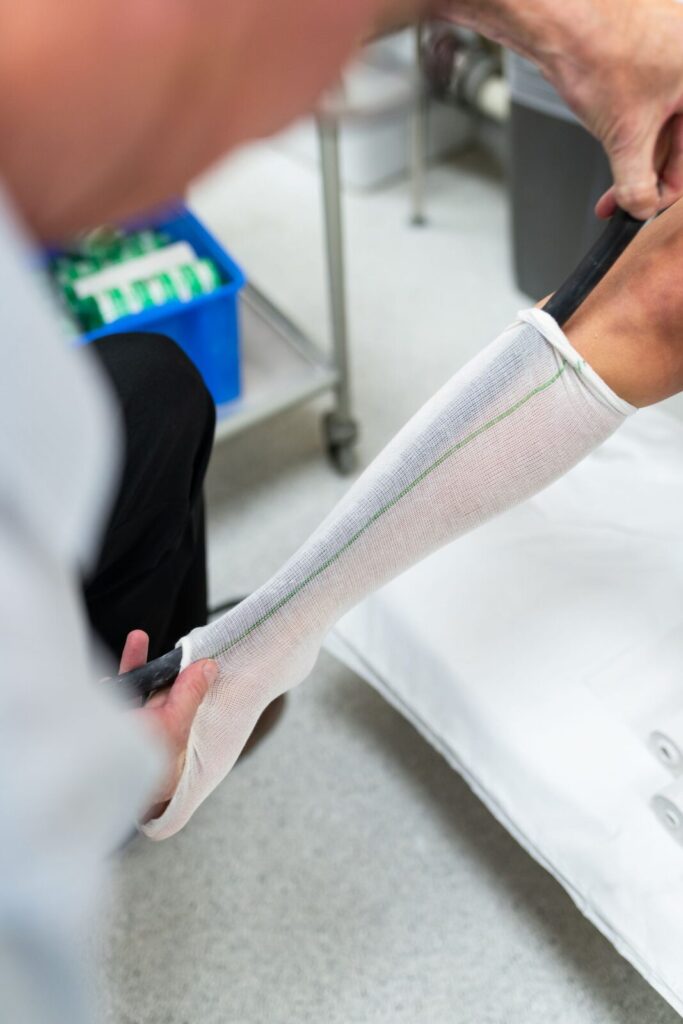 A white tubular compression sleeve being fitted onto a lower leg with an applicator