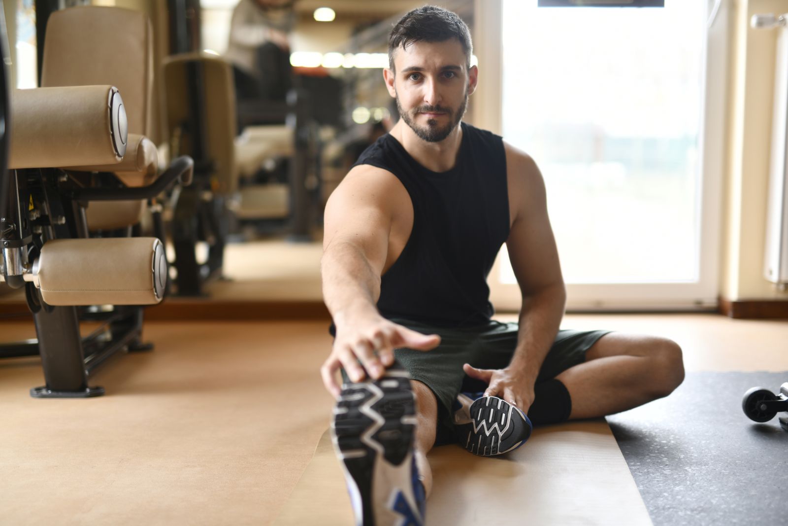 A man in gym clothes stretches on the floor in a modern fitness center