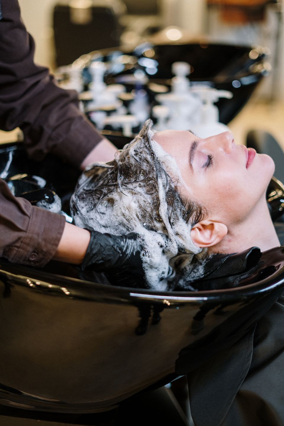 Hair stylist massaging shampoo into a client's scalp at a salon sink