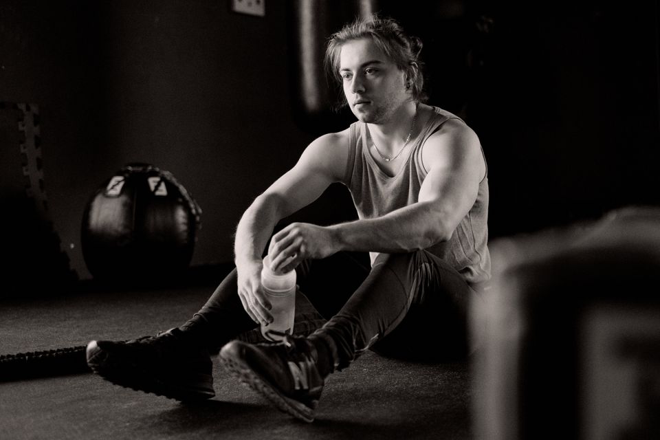 A young man sitting in a gym, resting after an intense workout session, holding a water bottle