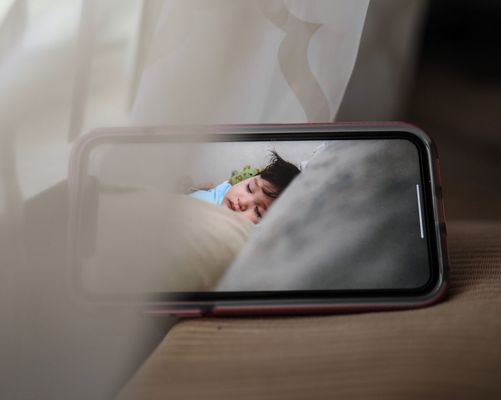 Smartphone displaying a live video feed of a sleeping baby in a crib