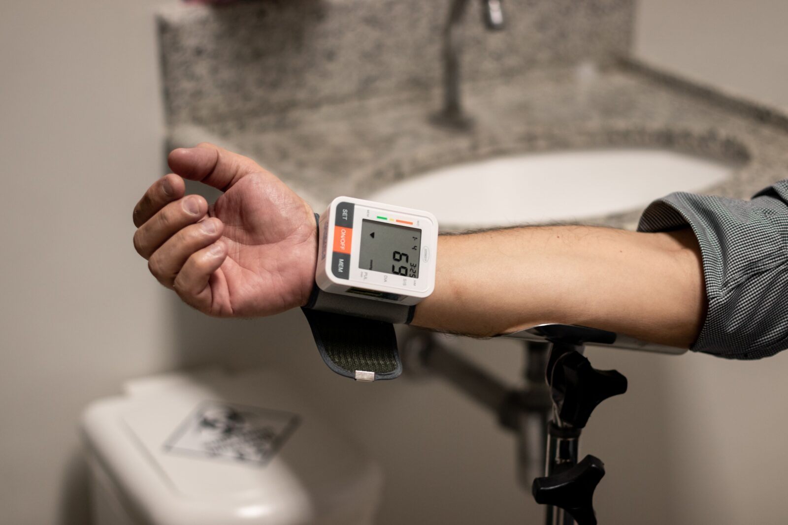 A close-up of an arm with a digital wrist blood pressure monitor wrapped around the wrist showing a reading