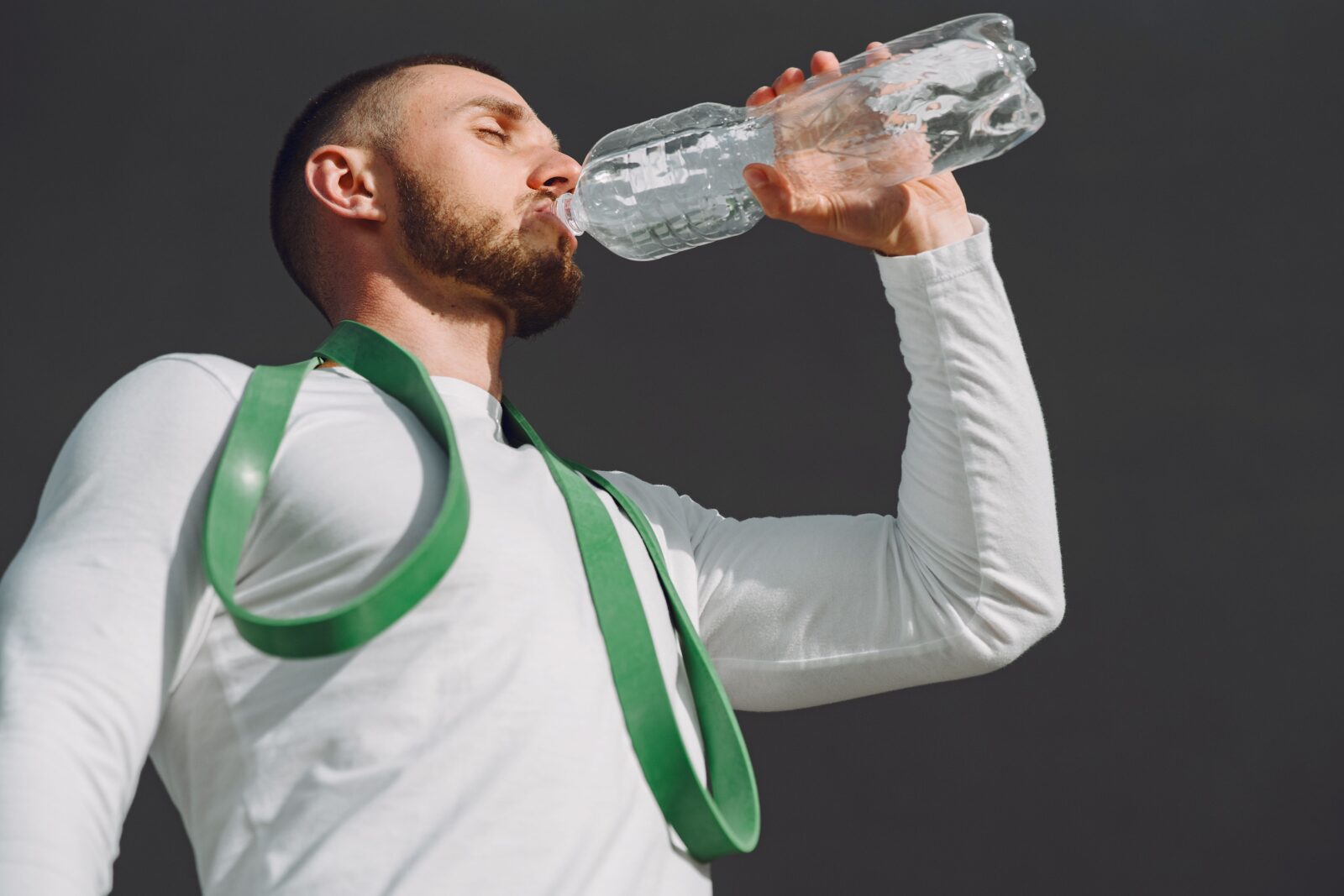 A fit man in sportswear drinking from a water bottle outdoors against a blue sky