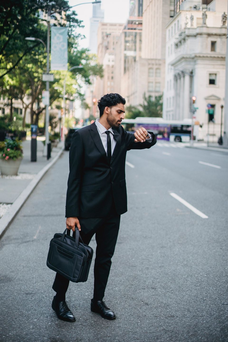 Businessman in black suit checking time while standing on a city street
