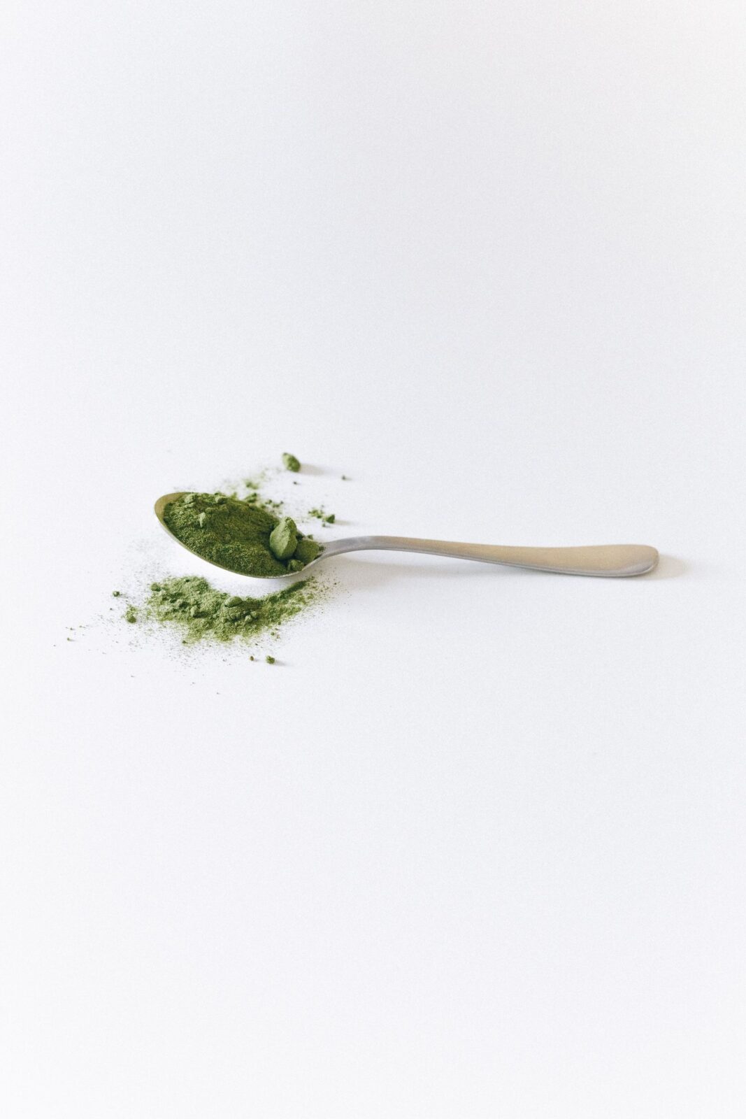 Close-up of a spoon holding fine green supplement powder on a white surface