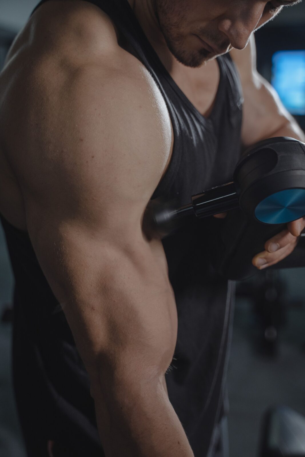 Close-up of a muscular arm being treated with a handheld massage gun