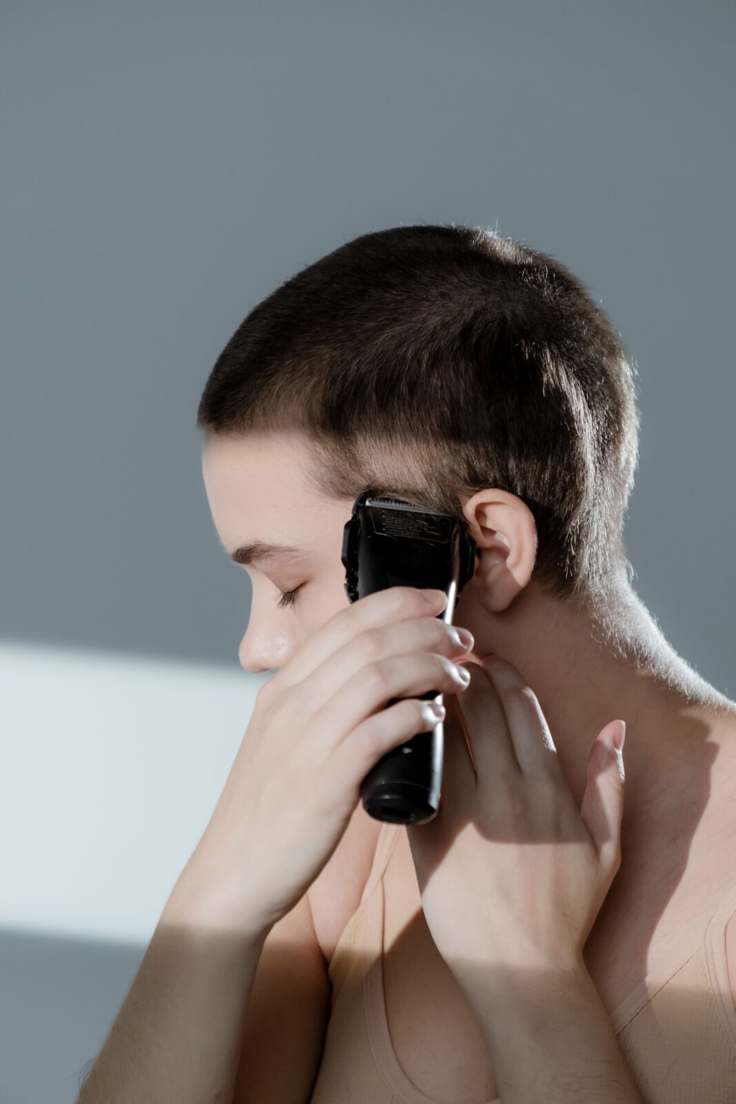 Woman using an electric hair clipper along her hairline above her ear