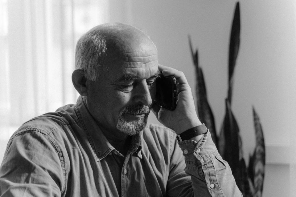 An elderly man having a phone conversation indoors, grayscale portrait
