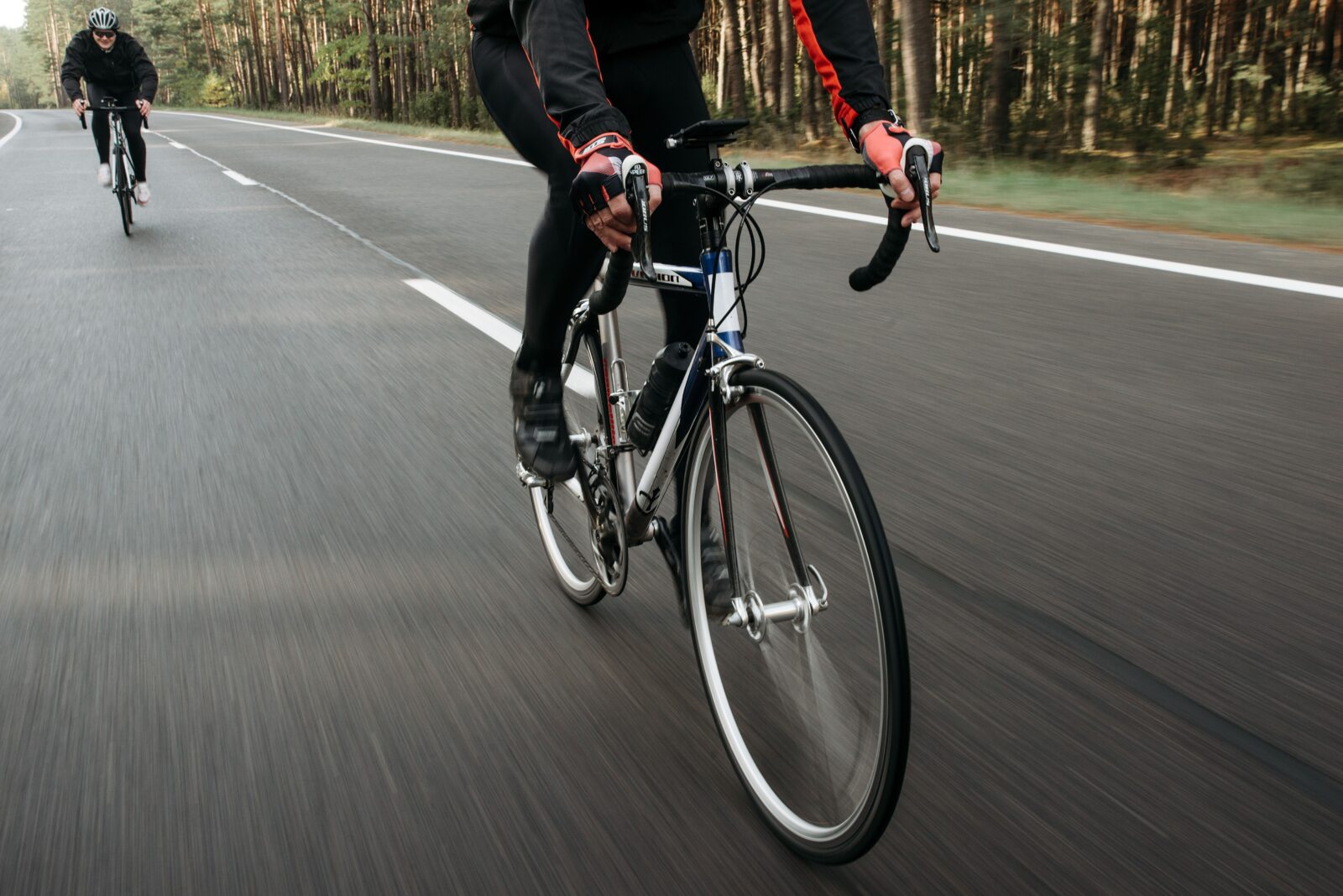 Multiple cyclists wearing helmets riding on a tree-lined road