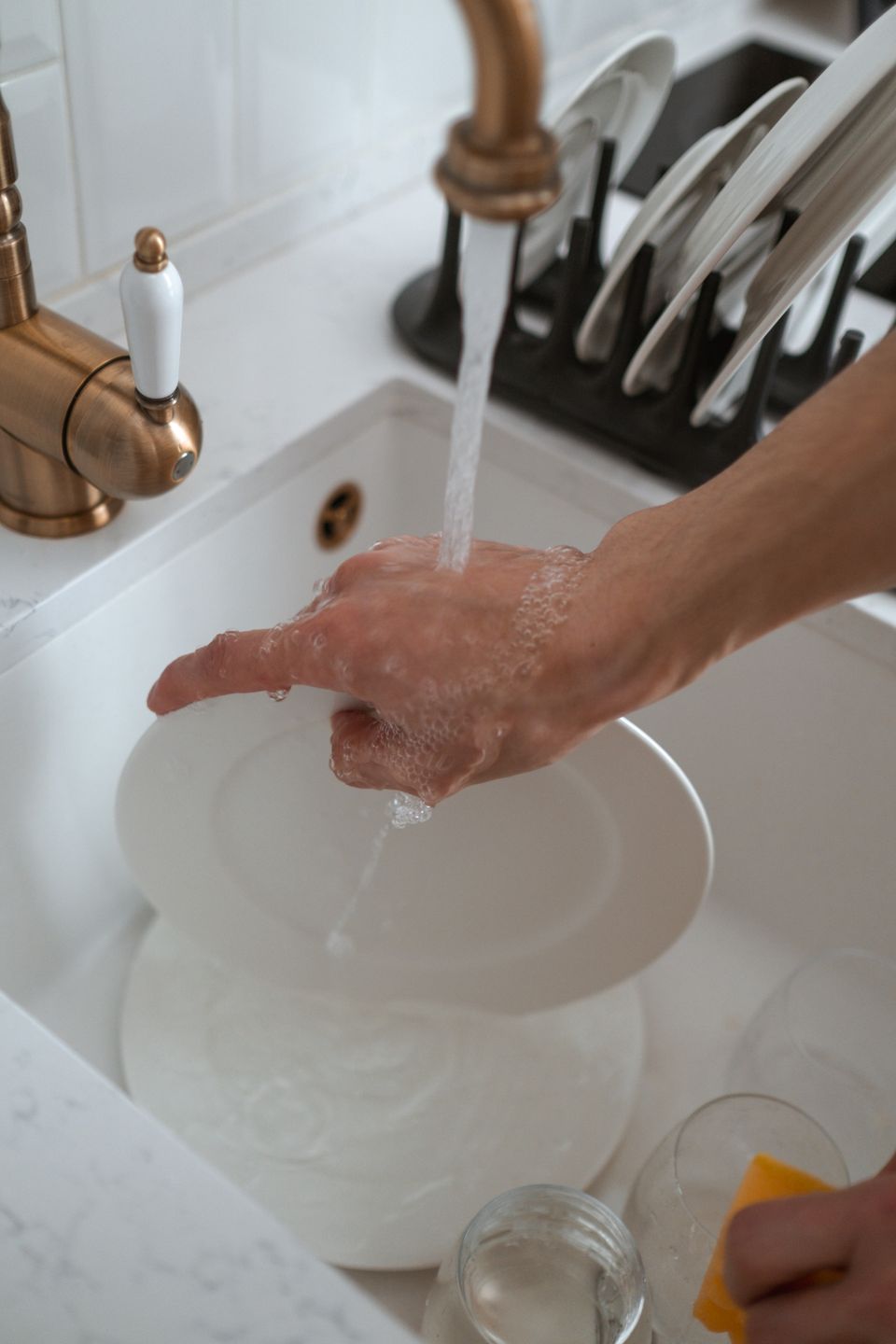 Close-up of hands washing dishes under running water in a kitchen sink