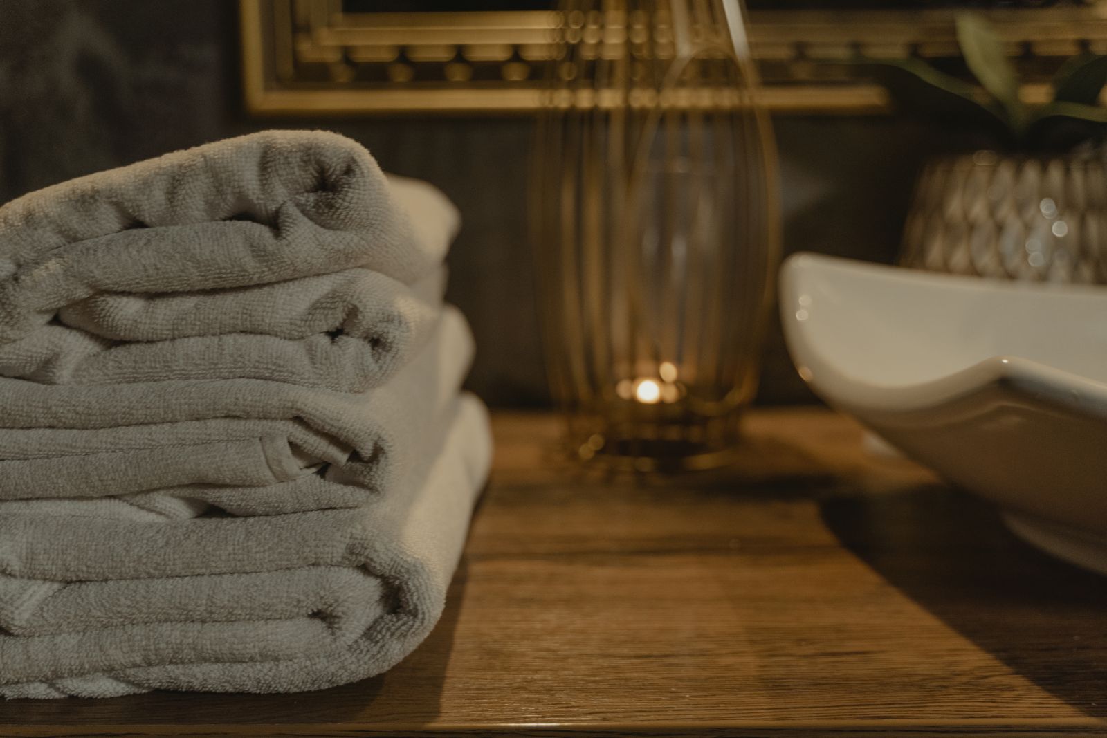 Neatly folded spa towels beside a lit candle on a wooden countertop, evoking an at-home spa setup