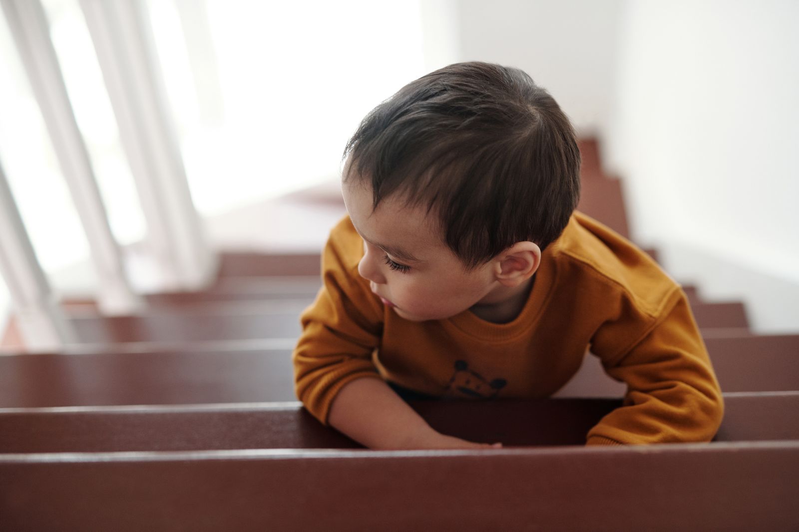 Young child in a yellow sweatshirt climbing a wooden staircase indoors