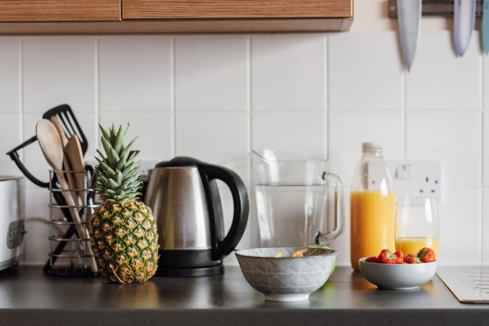 A kitchen counter with a whole pineapple, a bowl of strawberries, and a bottle of fresh juice