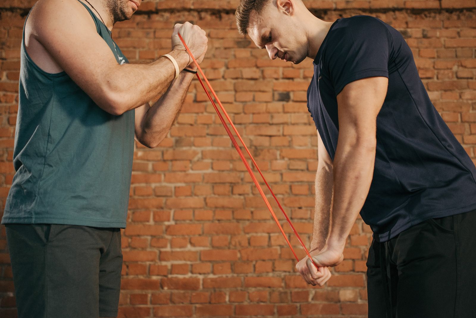 Two people facing each other, each gripping one end of a tube-style resistance band during a workout