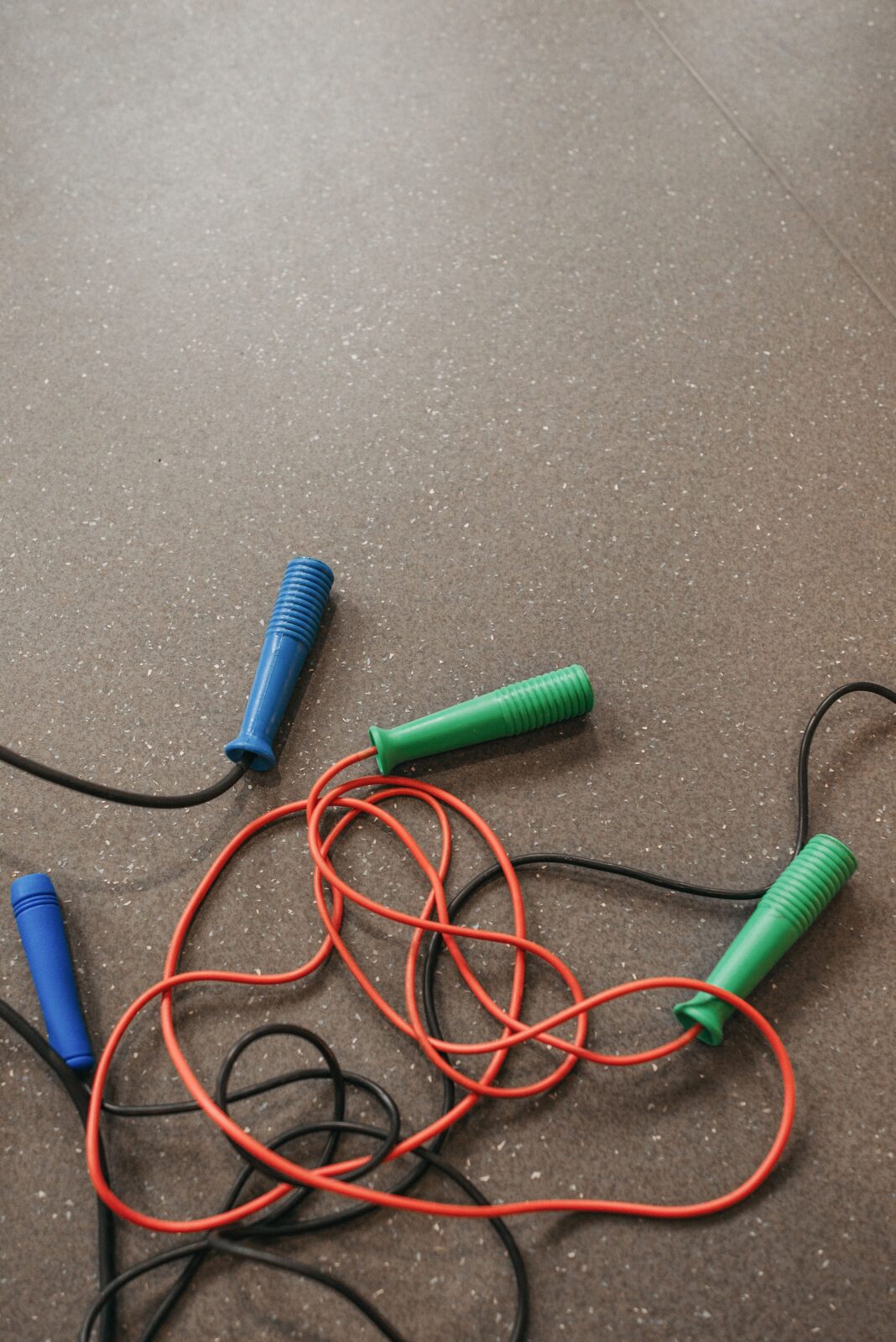 Close-up of tangled jump ropes with blue and green handles on a gym floor