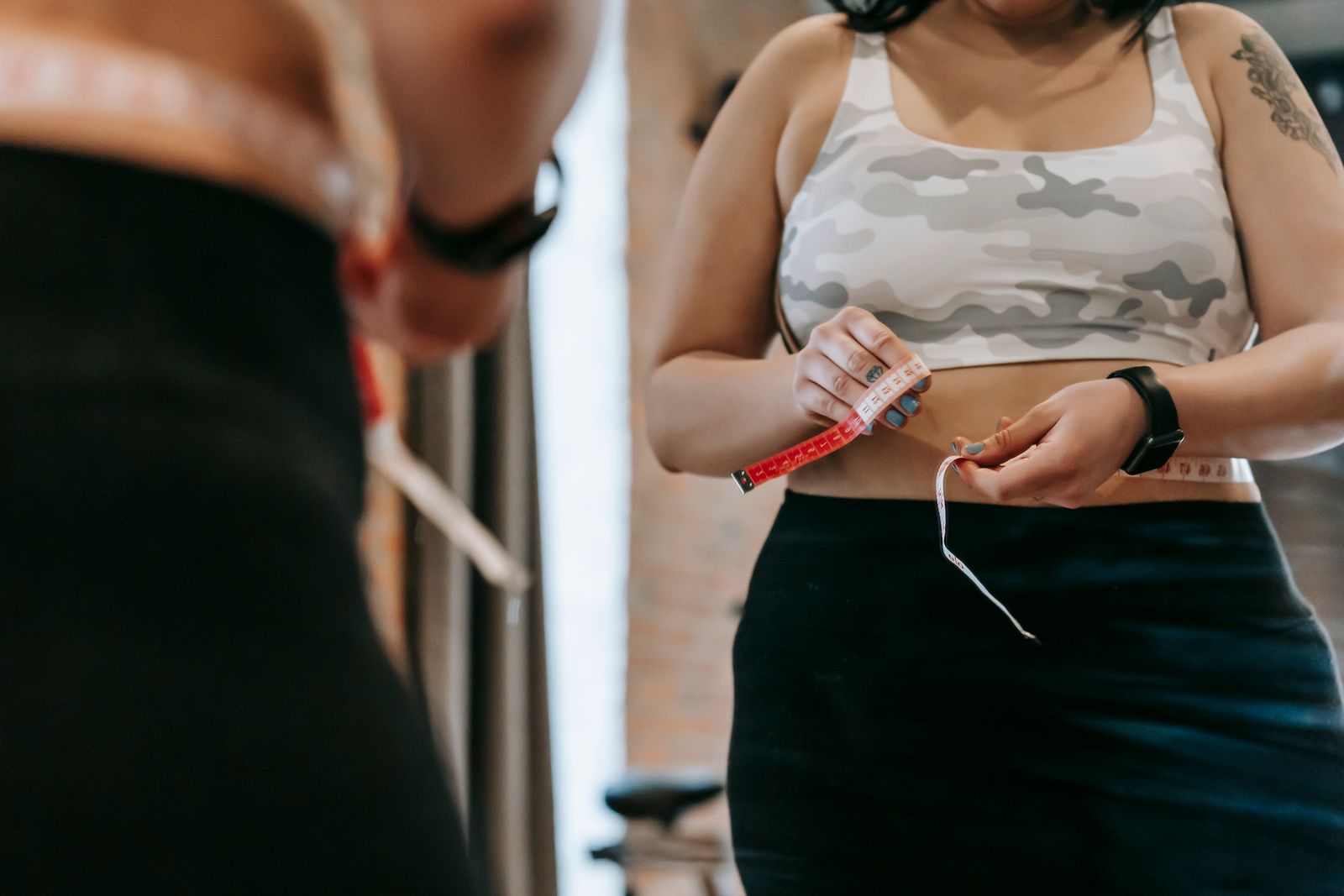 Person in activewear measuring their waist with a tape measure