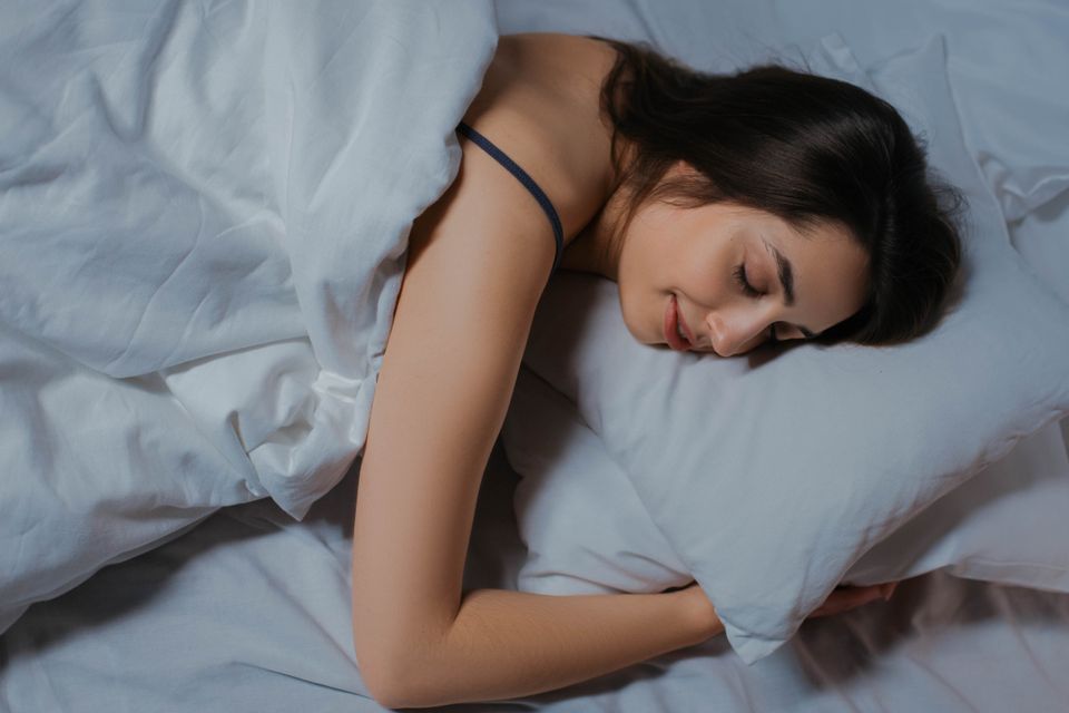 Woman sleeping peacefully in a cozy bed with white linens