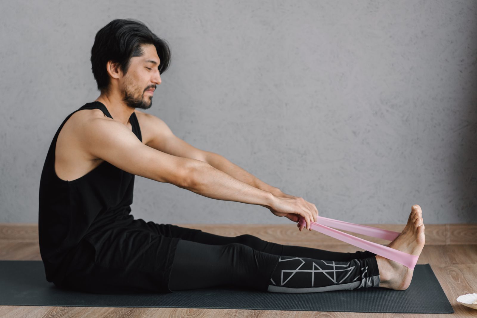 A man seated on a yoga mat using a loop resistance band to stretch his foot and ankle
