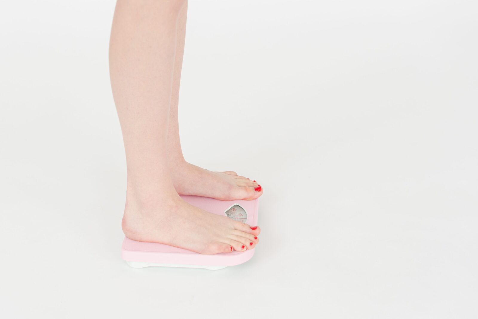 Close-up of bare feet standing on a bathroom scale against a white background