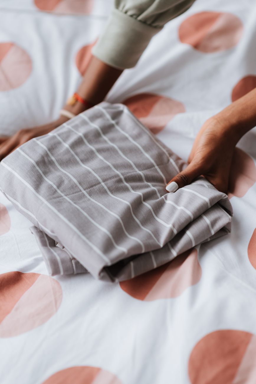 Person folding textured grey-and-white striped linen bed sheets