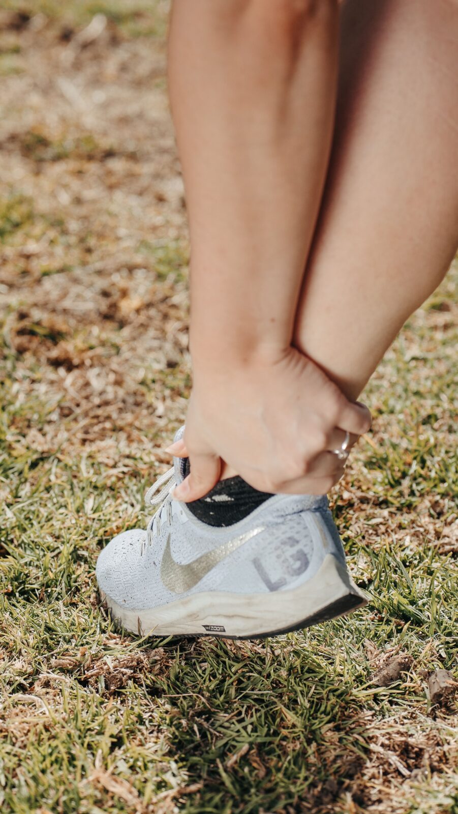 A close-up of a person holding their ankle while standing on grass, suggesting joint discomfort