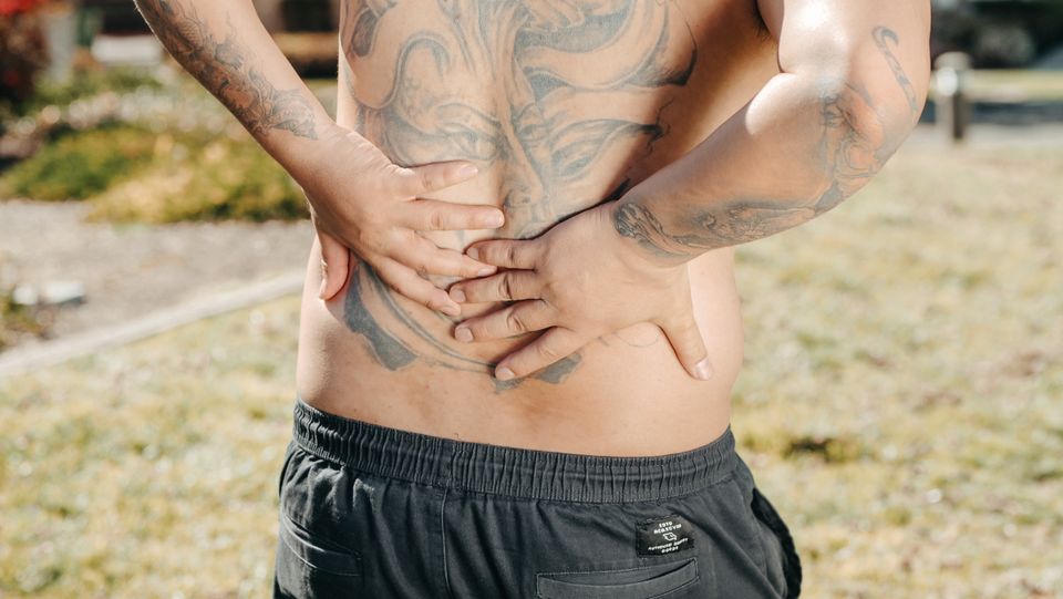 A man holding his lower back, showing signs of discomfort, outdoors