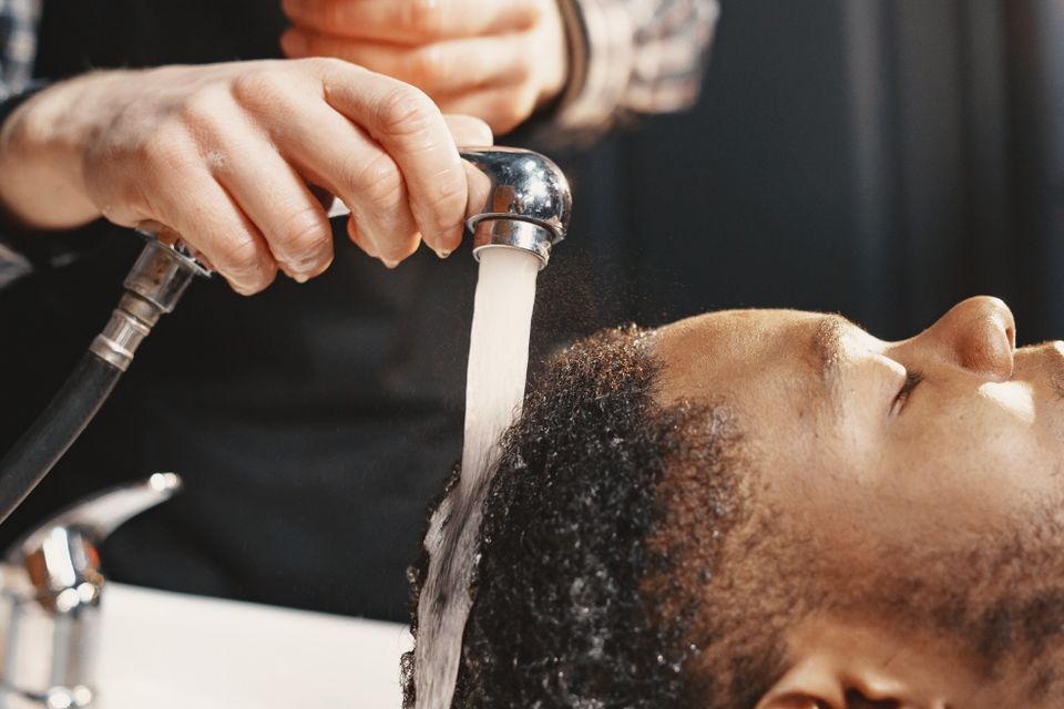 Person washing a man's curly hair at a sink, working fingers into the scalp