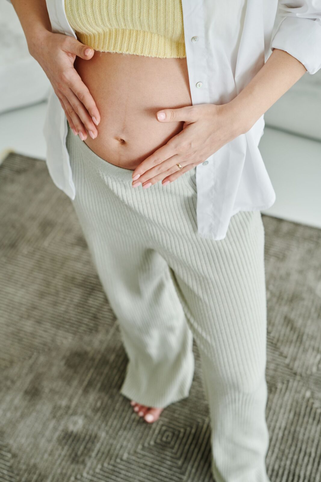Close-up of a pregnant person resting both hands on their belly