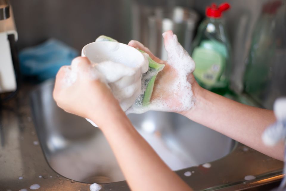 Hands washing a shaker cup with soap suds in a kitchen sink