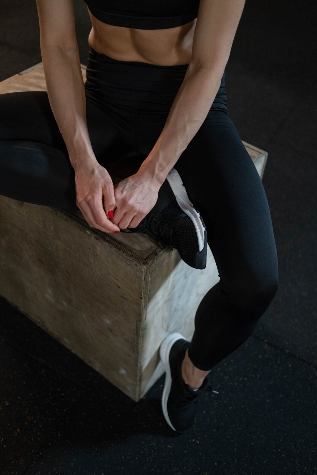 A muscular woman in black athletic wear sitting on a plyometric box resting between exercises