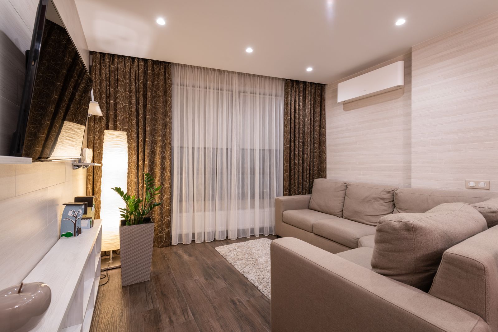 A stylish, cozy living room with a sofa, wood flooring, and soft natural lighting