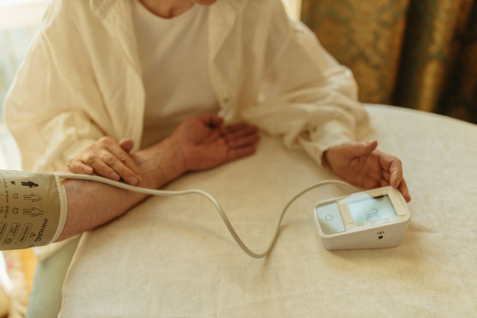 Senior adult checking blood pressure with a traditional digital arm cuff monitor at home