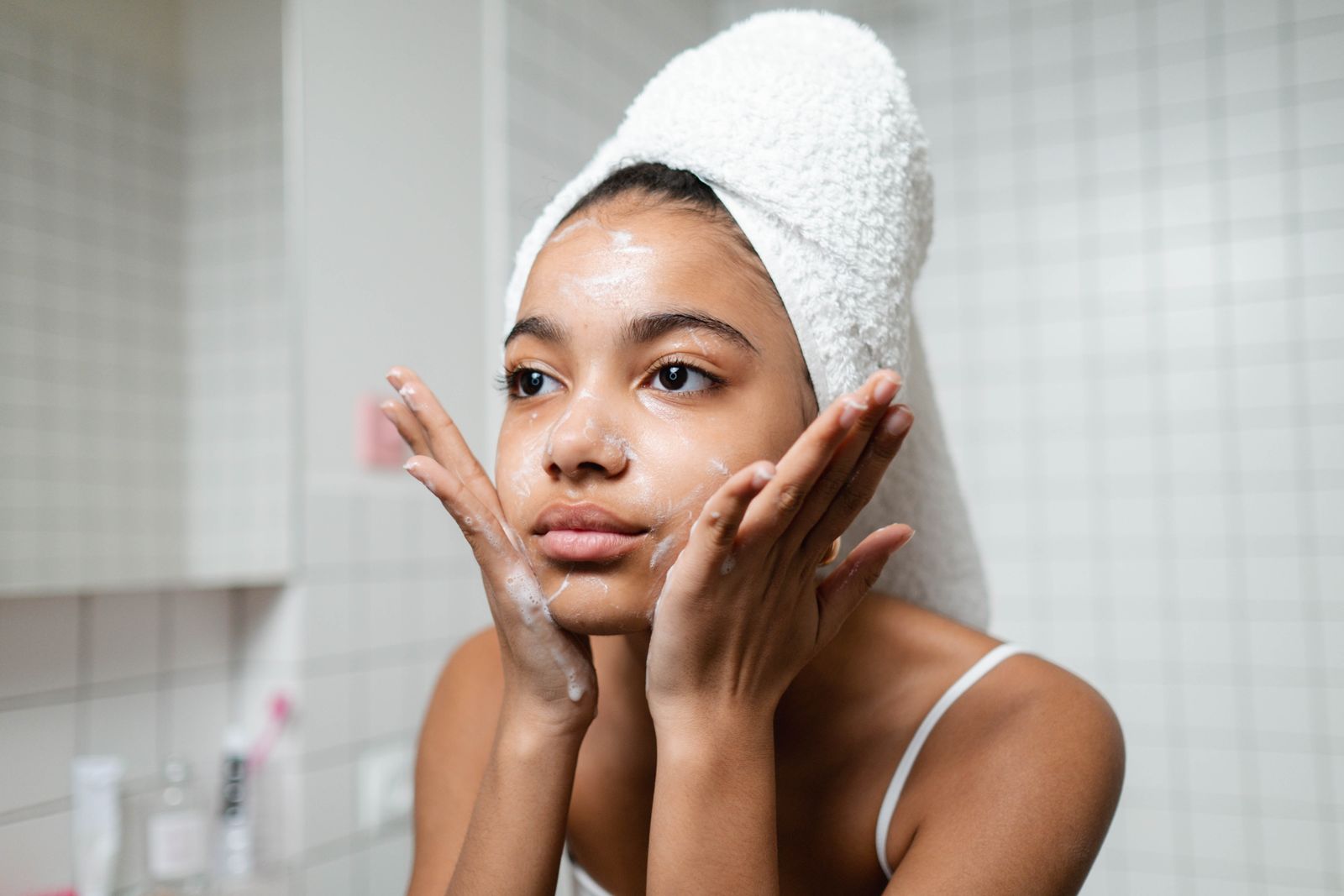 Woman with a towel wrapped around her head washing her face at a bathroom sink