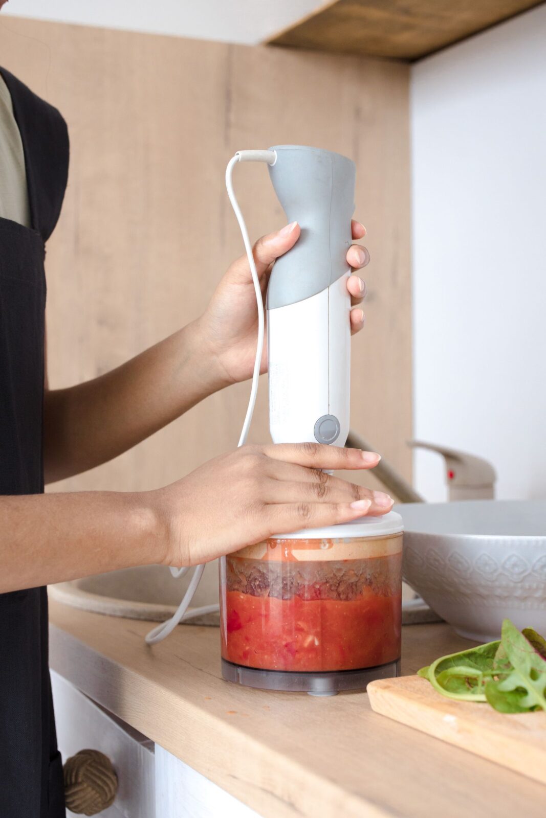 A hand blender pureeing chopped vegetables in a pot, close-up on the blending wand and blade.