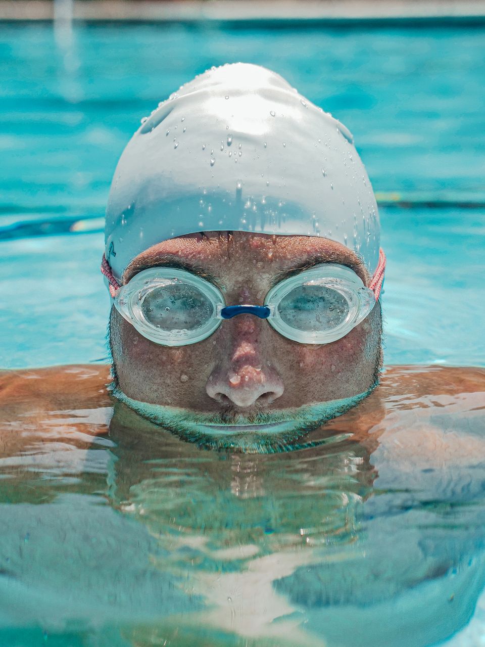 A male swimmer training in a pool wearing goggles and a swim cap