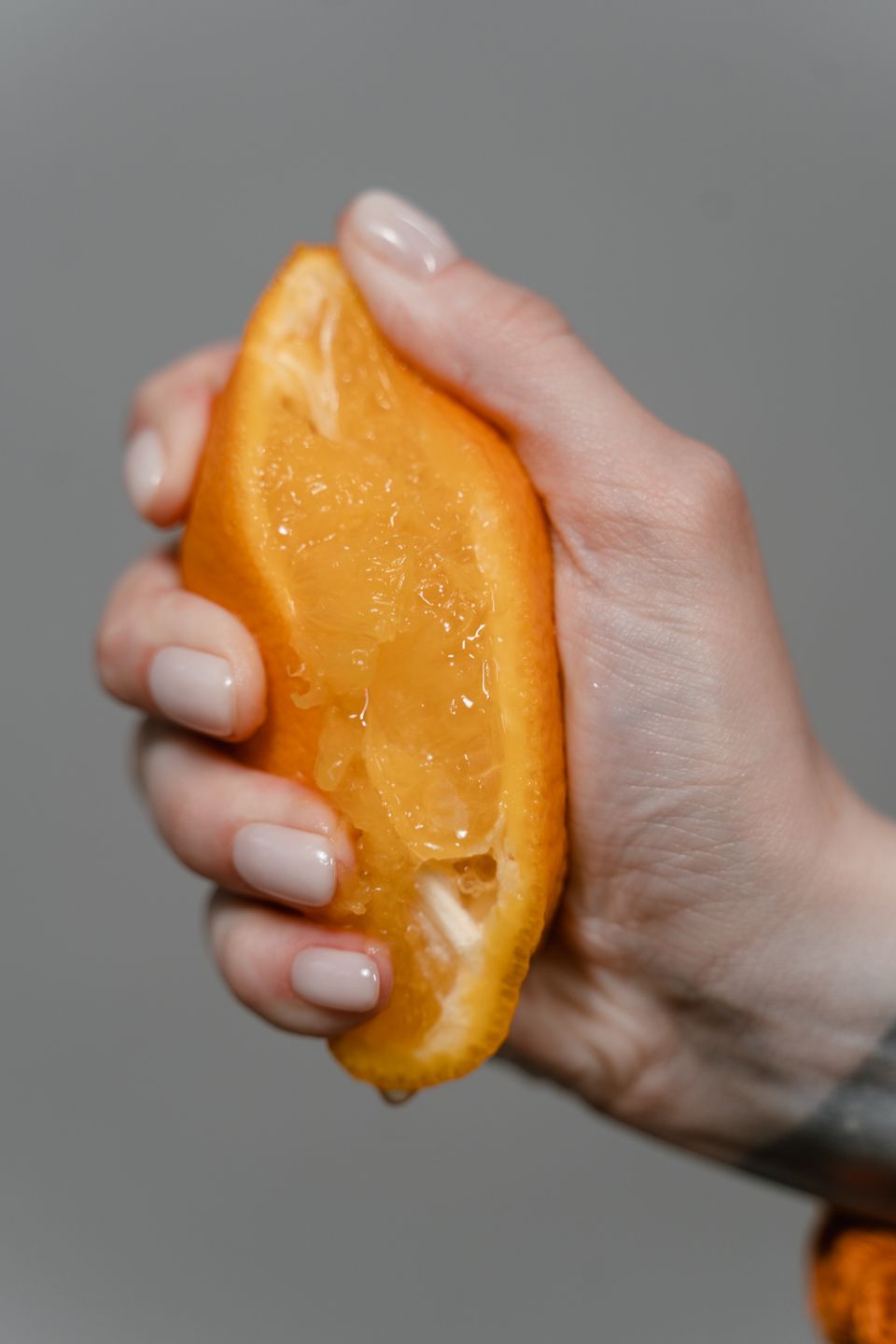Close-up of a hand squeezing a halved orange with juice dripping out
